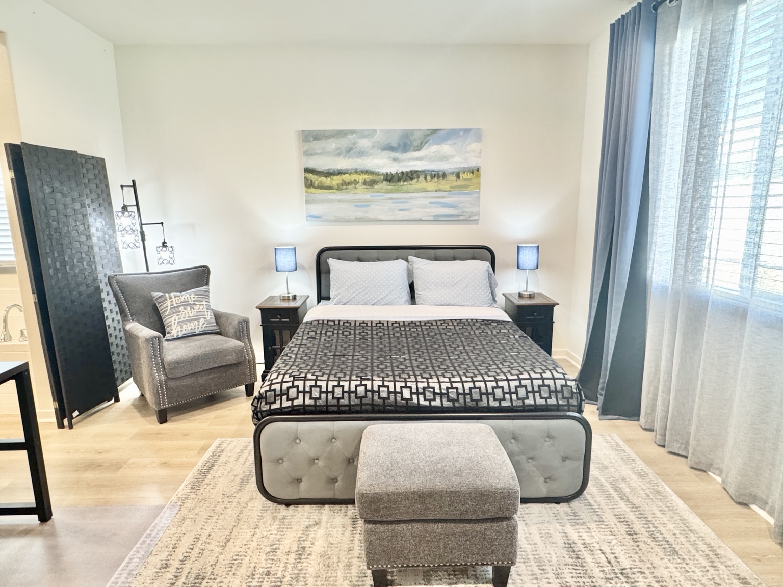 Platinum bedroom with queen bed, armchair, ottoman, and blue curtains